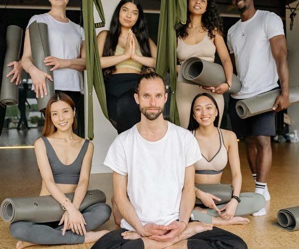 Diverse group of people smiling and preparing for a yoga class in a studio.